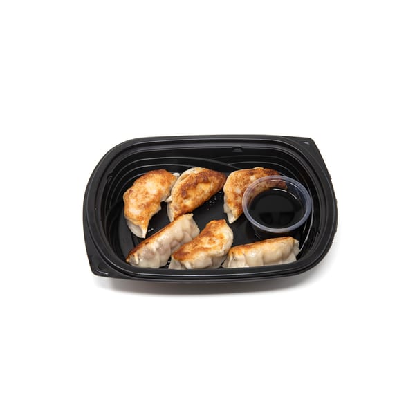 Six pan-fried Chinese dumplings with a side of soy sauce in a black takeout container.