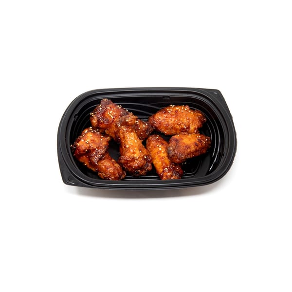 Imperial Chinese chicken wings, glazed and topped with sesame seeds, in a black takeout container.